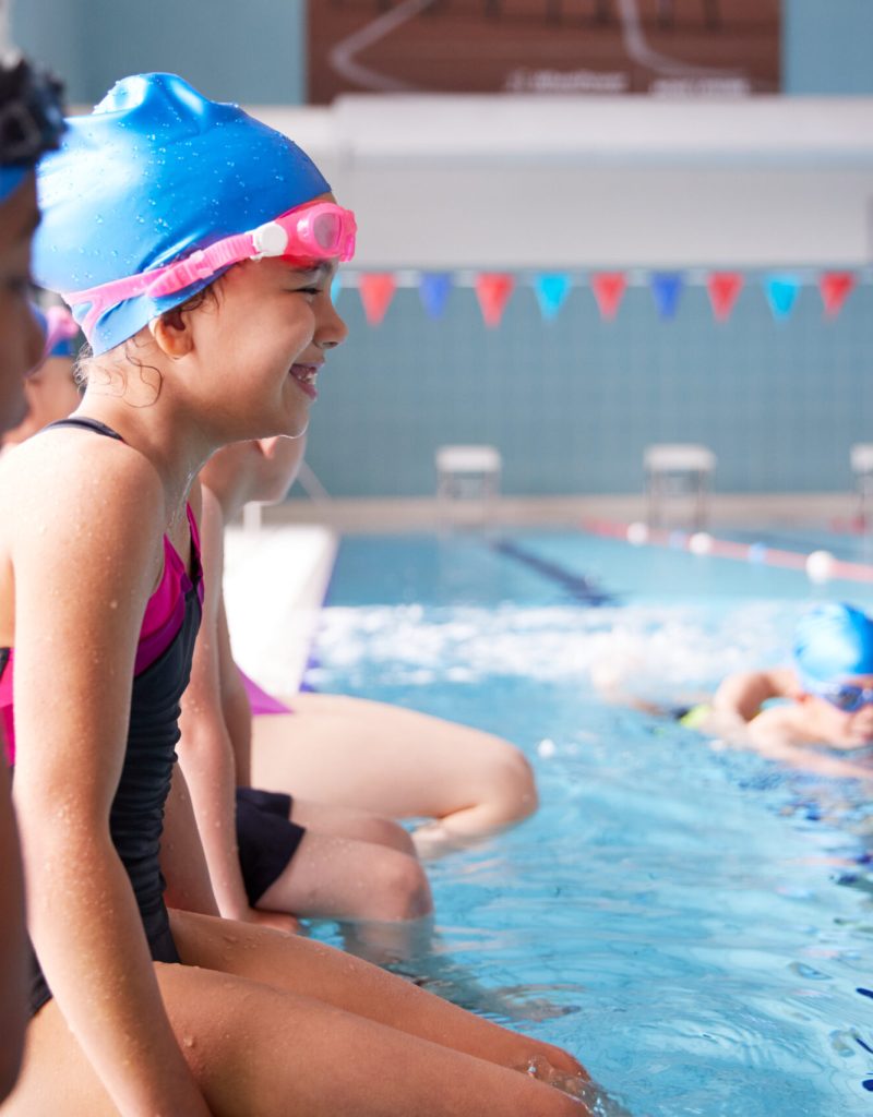 Male Coach In Water Giving Group Of Children Swimming Lesson In Indoor Pool