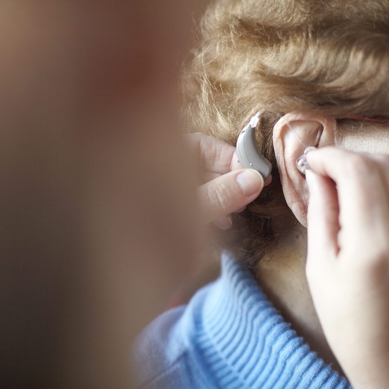 Mature woman helping senior woman insert hearing aid, close-up, differential focus